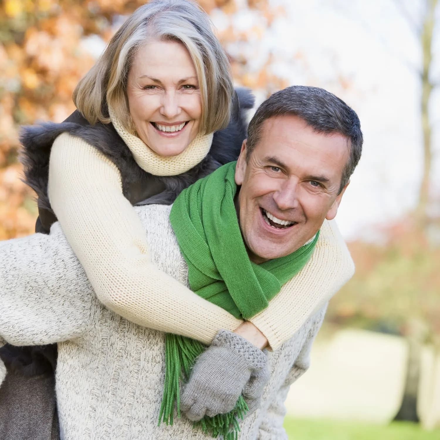 Smiling couple in autumn — piggyback embrace with green scarf